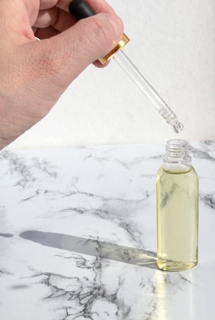 Close up of serum in dropper in front of a skin care product.