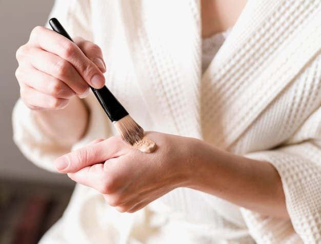 A hand holding a foundation brush applying liquid foundation to a clean face, showing the texture of the bristles and the foundation blending into the skin.