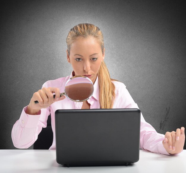 A person using a magnifying glass to examine a product review on a laptop screen, symbolizing the act of scrutinizing reviews for authenticity.